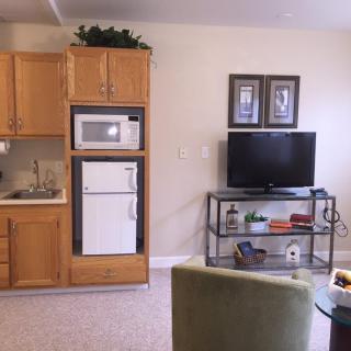 A cozy living area with a small kitchen, featuring a microwave, refrigerator, and television.