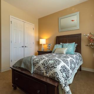 A cozy bedroom with a neatly made bed featuring patterned bedding, a bedside lamp, and a decorative mirror on the wall.