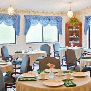 A well-arranged dining room with multiple tables and chairs, featuring blue curtains and elegant table settings.