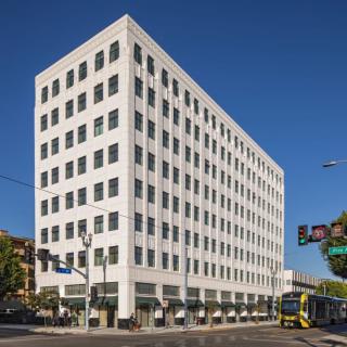 A modern office building on a city street corner under a clear blue sky.
