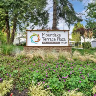 A sign for Mountlake Terrace Plaza surrounded by lush greenery and trees.