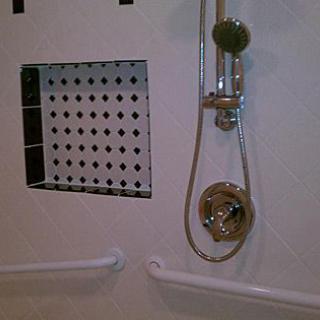 A bathroom shower with a handheld showerhead, tiled wall niche, and grab bars.