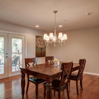 A cozy dining room with a wooden table set and a chandelier, featuring hardwood floors and French doors leading outside.