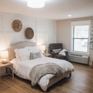 A cozy and modern bedroom with neutral tones, featuring a comfortable bed, decorative pillows, wooden flooring, and ambient lighting.
