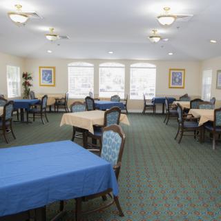 A spacious dining area with multiple tables and chairs, featuring large windows and framed artwork on the walls.