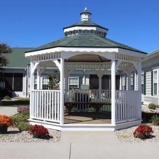 A white gazebo with a green roof surrounded by flowers and a paved path.