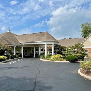 A scenic view of a building entrance with a driveway surrounded by lush greenery and a partly cloudy sky.
