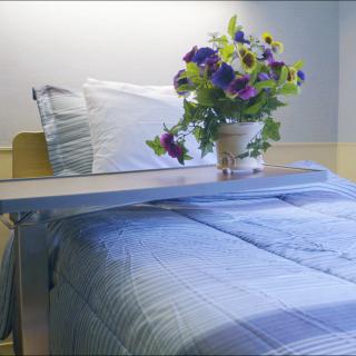 A hospital bed with a bouquet of flowers in a vase on the tray table.