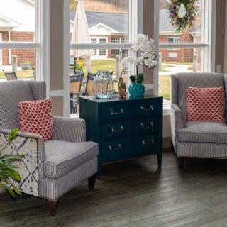 A cozy living room setup with two armchairs, a side table, and decorative cushions near large windows.