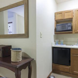 Compact kitchen area with wooden cabinets, a microwave, and a sink adjacent to a small table and mirror.
