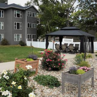 A landscaped garden area with colorful flowers and a gazebo, situated near an apartment building.