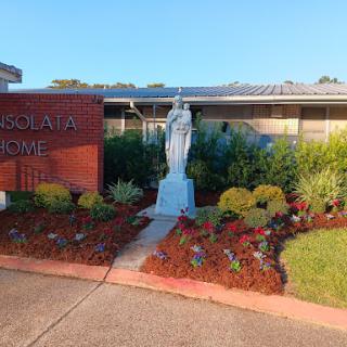 A serene view of a statue surrounded by vibrant flowers at the entrance of a building.