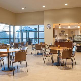 An empty cafe interior with tables and chairs, featuring large windows allowing natural light.