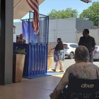 People are gathered in an outdoor waiting area, with one person in a wheelchair.