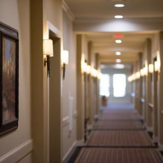 A well-lit hotel hallway with carpeted floors and artwork on the walls.