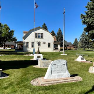 A collection of monuments and flags on a grassy lawn in front of a building on a sunny day.