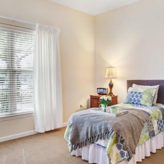 A cozy bedroom with a neatly made bed, a lamp on the nightstand, and a window with curtains.