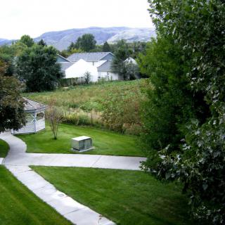 A scenic view of a pathway cutting through lush greenery with houses and mountains in the background.