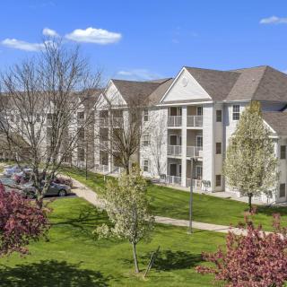 A scenic view of a residential apartment complex surrounded by greenery and trees under a clear blue sky.