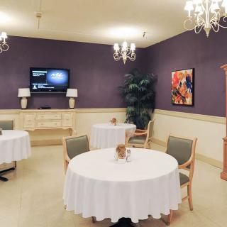 A well-decorated dining room featuring round tables with white tablecloths, elegant chandeliers, and a television.