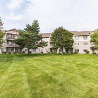 A residential apartment complex with a well-maintained lawn and surrounding trees.