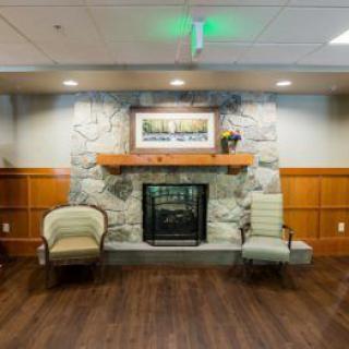 A cozy interior space featuring a stone fireplace, two chairs, and wooden flooring.