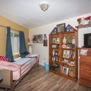 A cozy bedroom with a bed, bookshelf, and television set on a wooden floor.