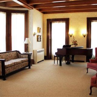 A classic-style living room featuring a sofa, armchairs, and a piano with large windows allowing natural light.