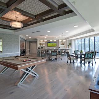 A stylish and spacious modern lounge area featuring a pool table, bar, and ample seating with large windows for natural light.