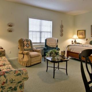 A cozy living room with a mix of traditional furniture and decor, featuring armchairs, a sofa, a bed, and a coffee table.