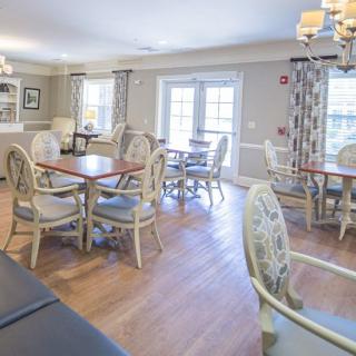 A bright and inviting dining area with multiple tables and chairs, featuring large windows and elegant chandeliers.