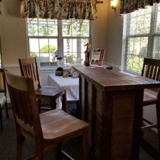 A cozy dining area with a wooden table and chairs, illuminated by natural light from the windows.