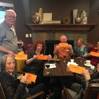 A group of people gathered indoors, sitting around a table and holding pieces of orange paper.