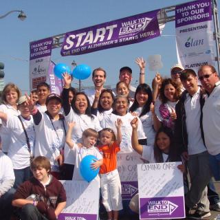 A group of people gathered at the start line of a charity walkathon, holding balloons and smiling.
