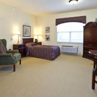 A cozy hotel room with a bed, armchair, and dresser.