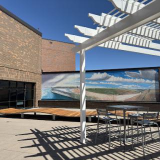 A sunny outdoor space featuring a wooden deck, modern architecture, and a vibrant mural in the background.