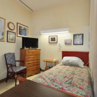 A cozy bedroom with a single bed, television, and various framed artworks on the wall.