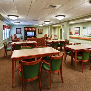 An empty dining area with wooden tables and chairs, carpeted flooring, and ceiling lights.