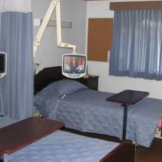 A hospital room with two beds, medical equipment, and a television.