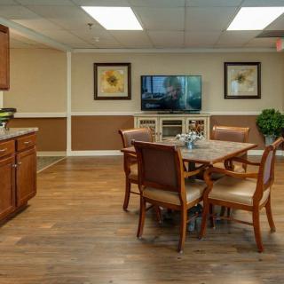 A cozy dining area with wooden flooring, featuring a table surrounded by chairs, a television on the wall, and decorative artwork.