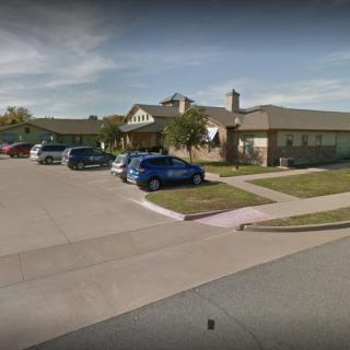 A suburban residential house with several cars parked in the driveway and a well-maintained lawn.
