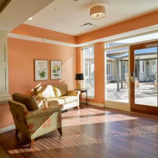 A cozy living room with a sofa and armchair, bathed in natural light from large windows.