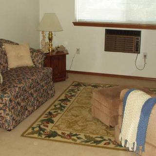 A cozy living room with a patterned sofa, an ottoman, and a floor lamp beside a window featuring an air conditioner.