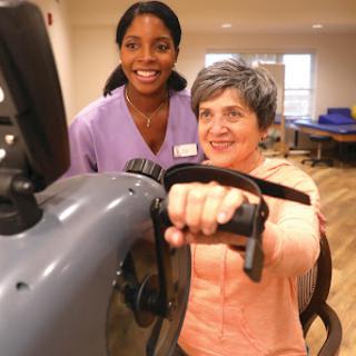 A healthcare worker assists an elderly woman during her exercise session in a rehabilitation center.