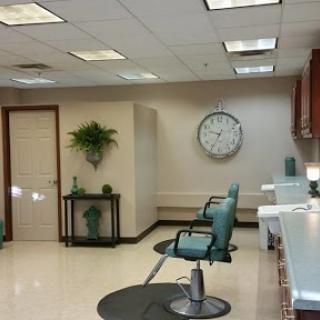 A tidy salon interior featuring comfortable chairs, decorative plants, and a wall clock.