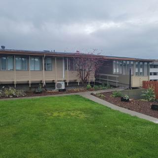 A modern building with large windows surrounded by a neatly maintained lawn and garden on an overcast day.