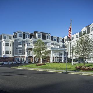 A residential building with multiple stories, featuring an American flag and surrounded by trees on a sunny day.