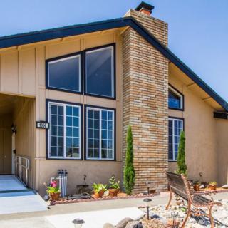 A modern house with large windows and a prominent brick chimney, surrounded by neatly arranged landscaping and outdoor seating.