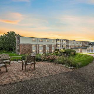 A serene outdoor view at sunset featuring a building, two chairs on a pathway, and lush greenery.
