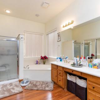 A spacious bathroom featuring a shower, bathtub, large mirror, and wooden vanity with multiple sinks.
